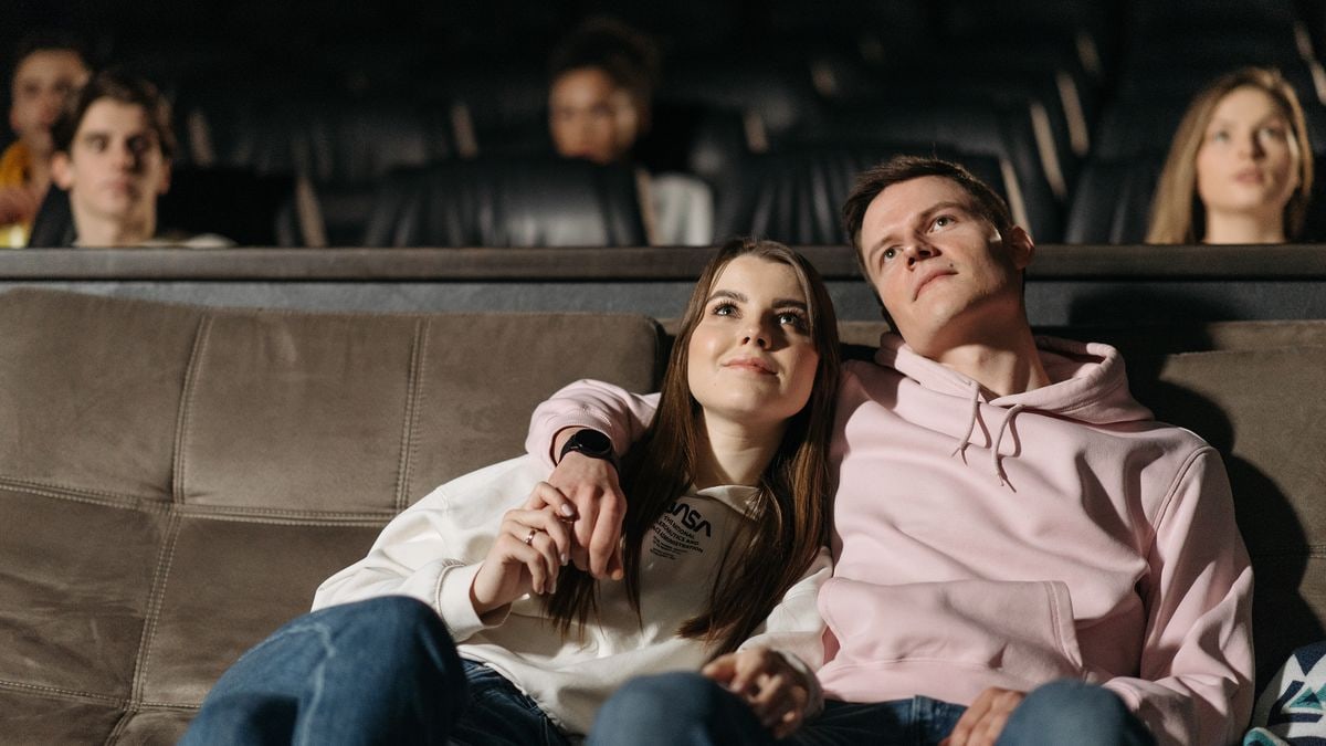 A happy couple sits closely in a theater enjoying a movie together.
